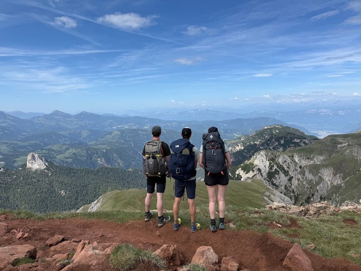 Three hikers with backpacks standing on a mountain summit overlooking a valley