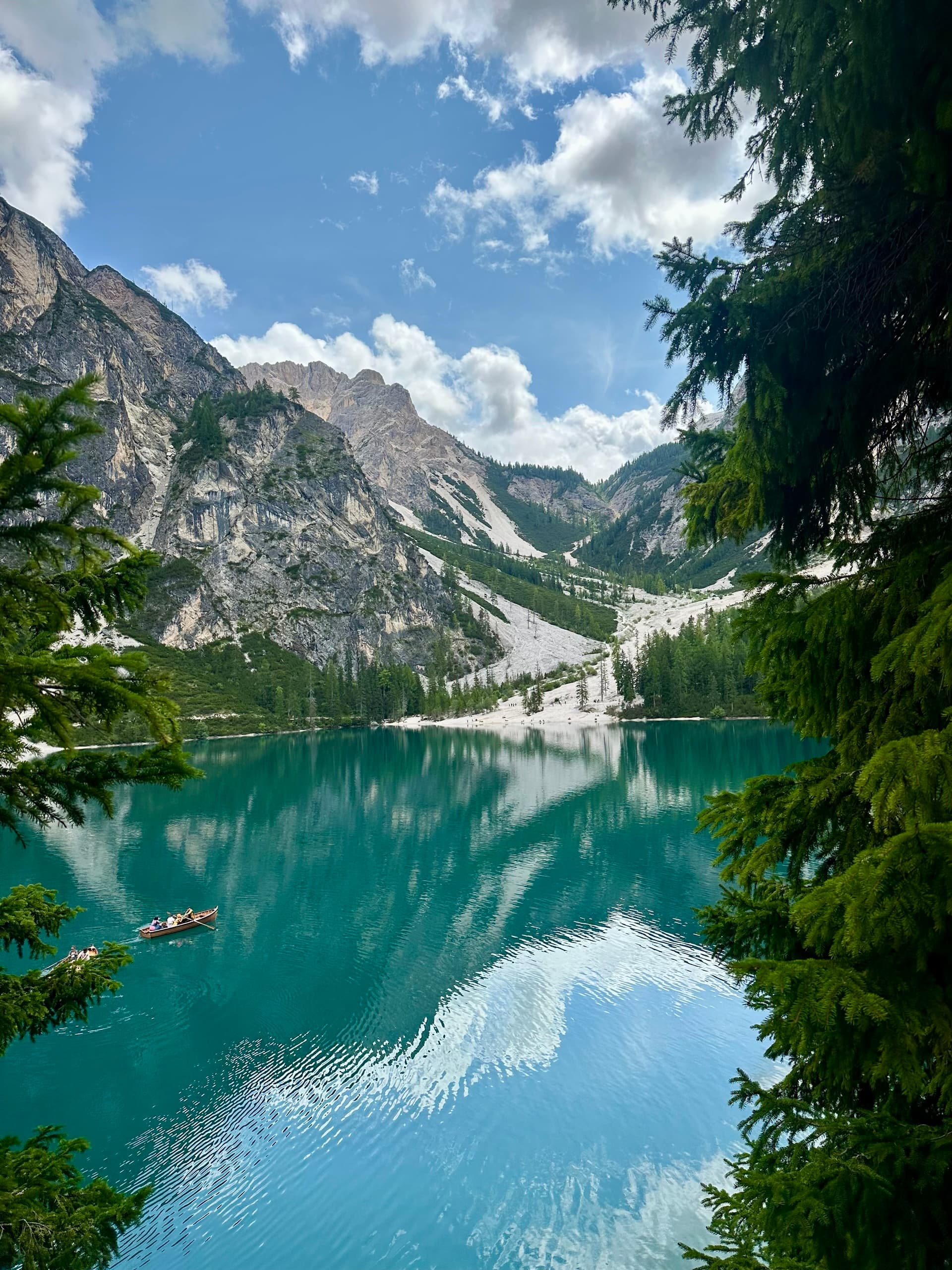 Turquoise alpine lake framed by trees with rowboats and mountains in the background