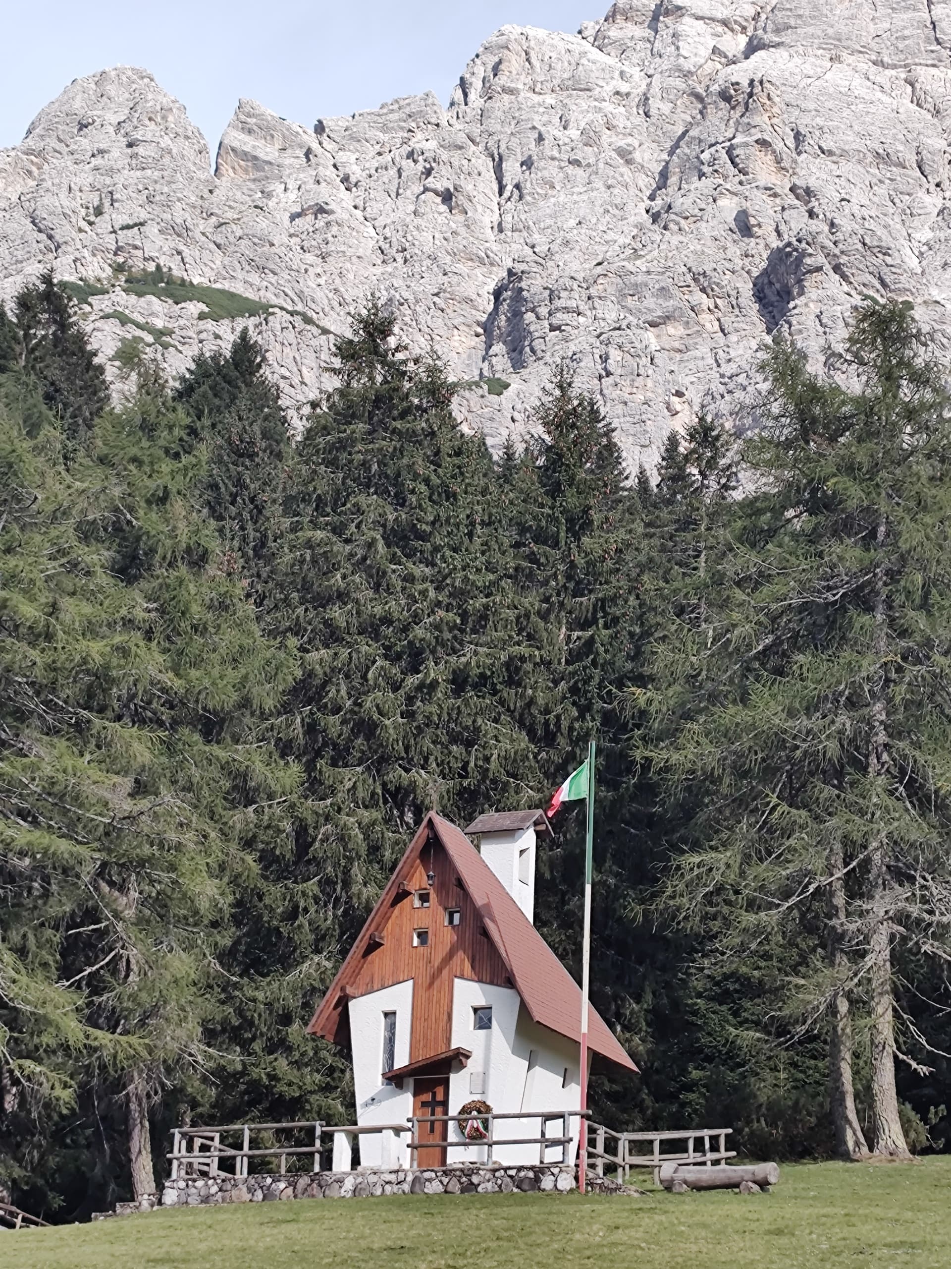 Small alpine chapel below rocky mountain cliffs and pine forest