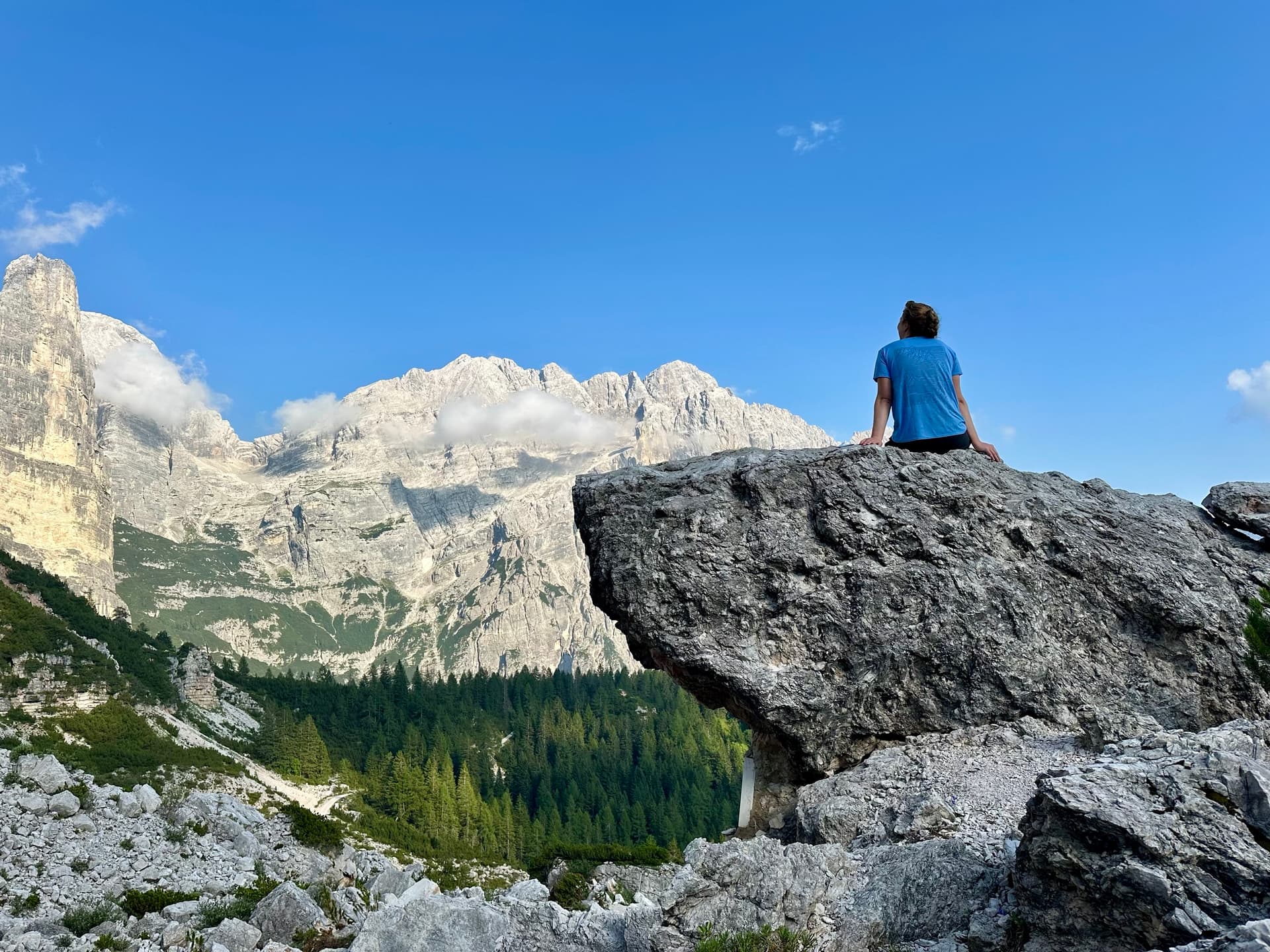Hiker sitting on a boulder overlooking a mountain valley and peaks