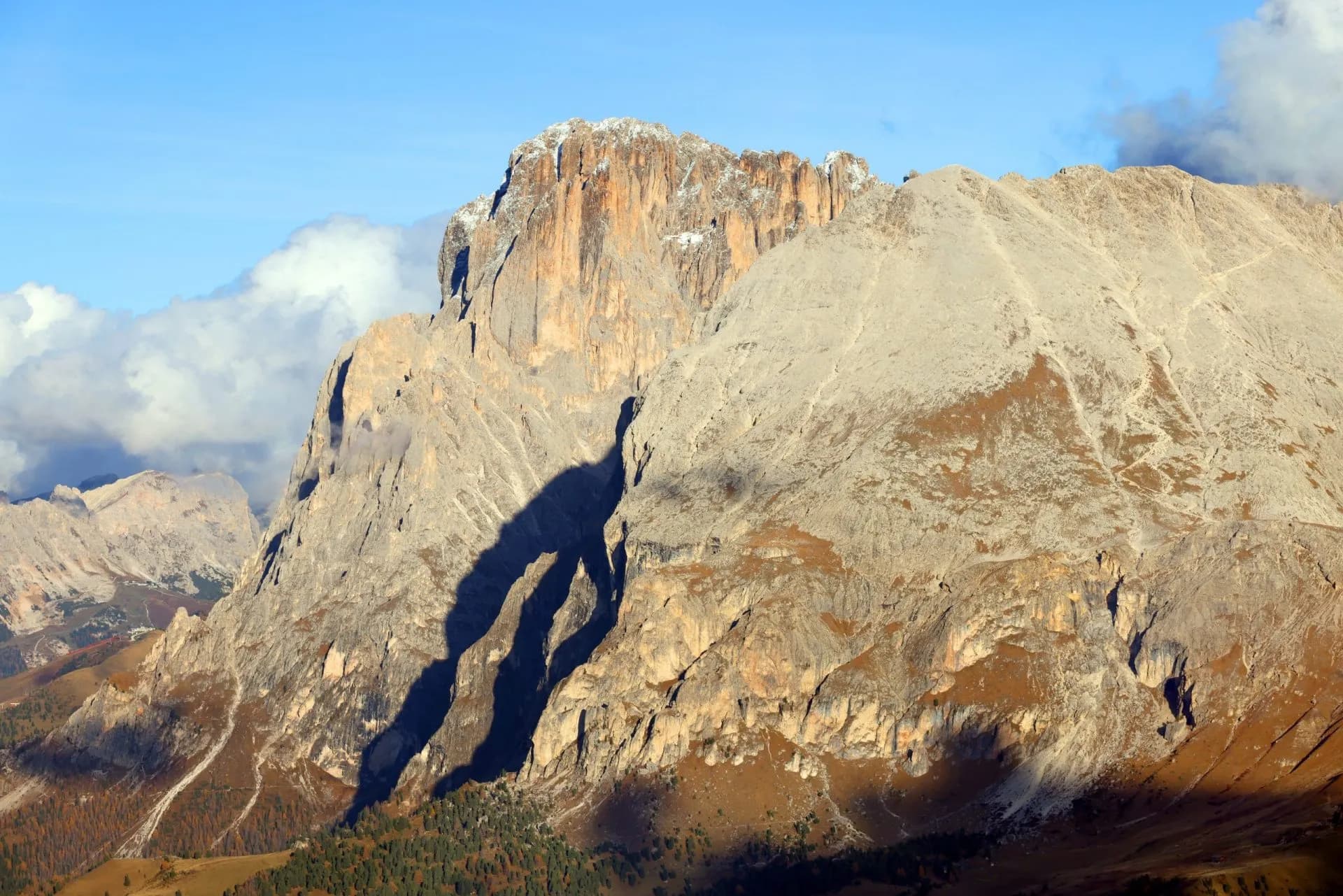 Massive rocky mountain face casting long shadows under a blue sky with white clouds, Plattkofel.