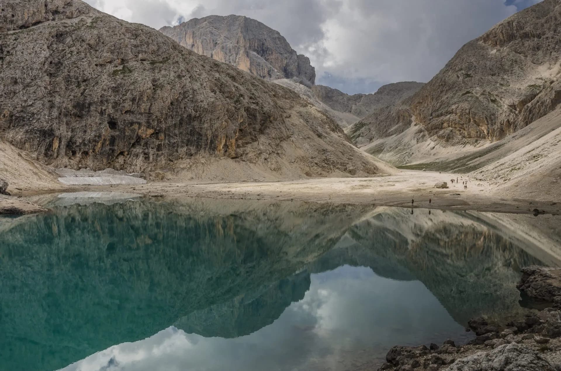 Alpine lake reflecting rugged mountains under a cloudy sky, Lake Antermoia visible