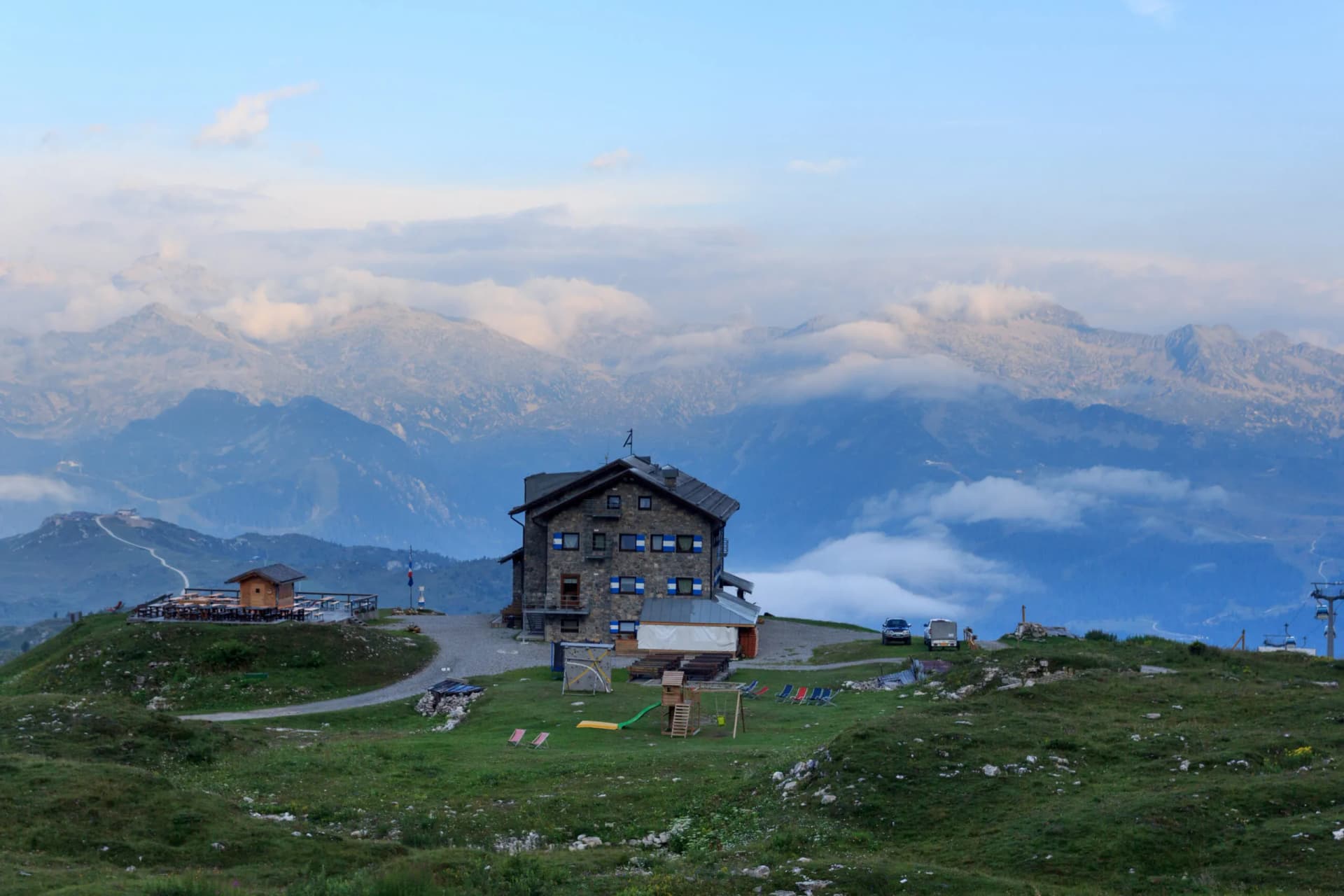 Rifugio Graffer stone mountain hut with panorama of Adamello Presanella Alps peaks shrouded in clouds.