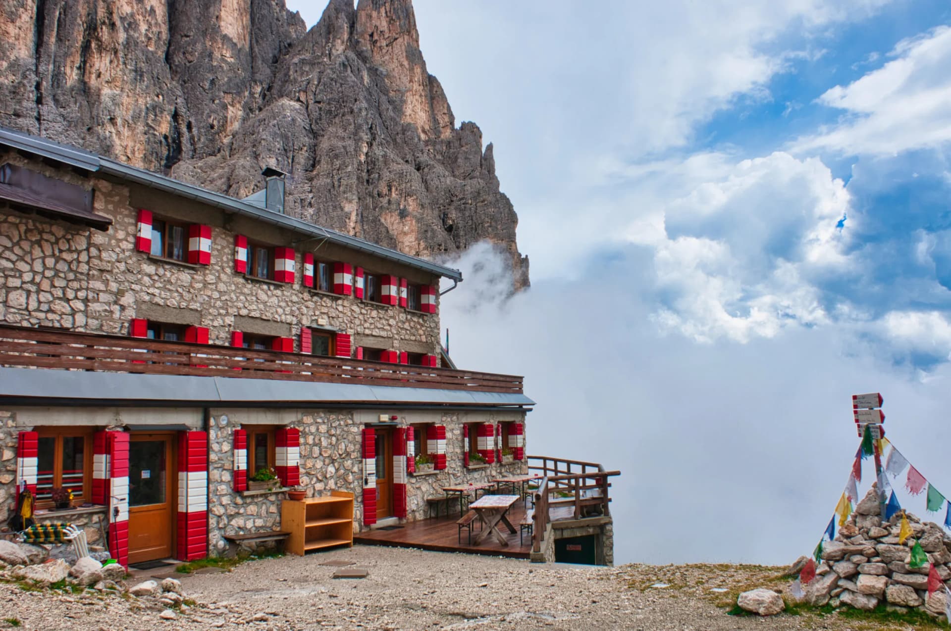 Rifugio Pradidali mountain hut with stone facade and red/white shutters against rocky peaks and clouds.
