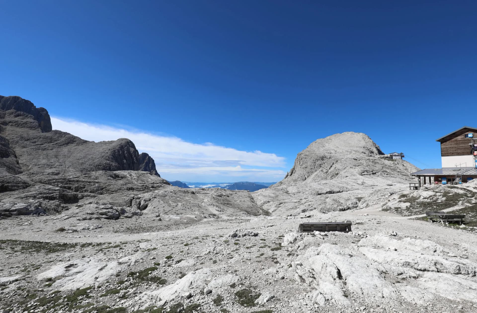 Rocky alpine terrain with Rifugio Rosetta building under a clear blue sky.