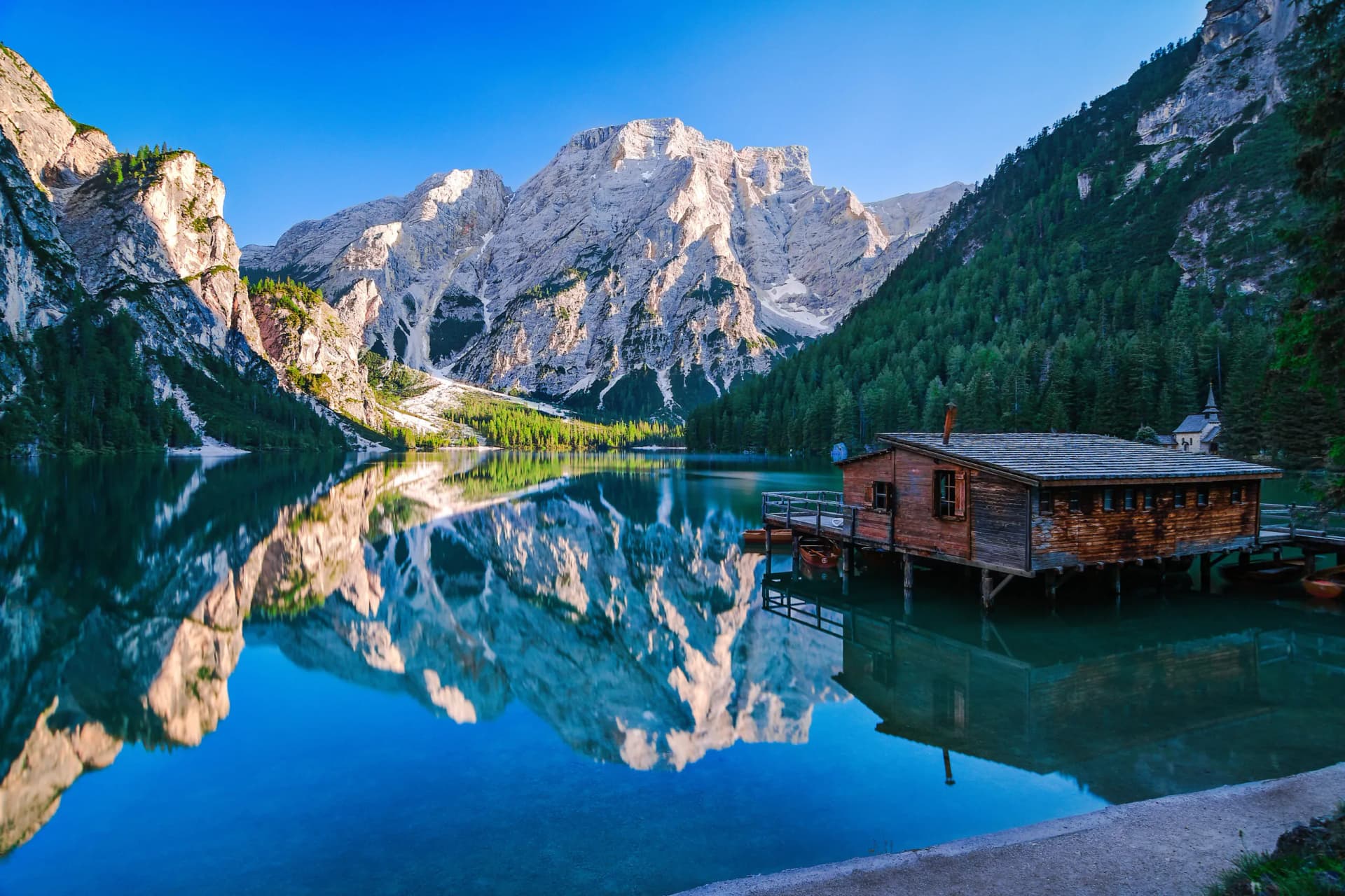 Lago di Braies wooden boathouse reflecting in alpine lake with massive mountains.