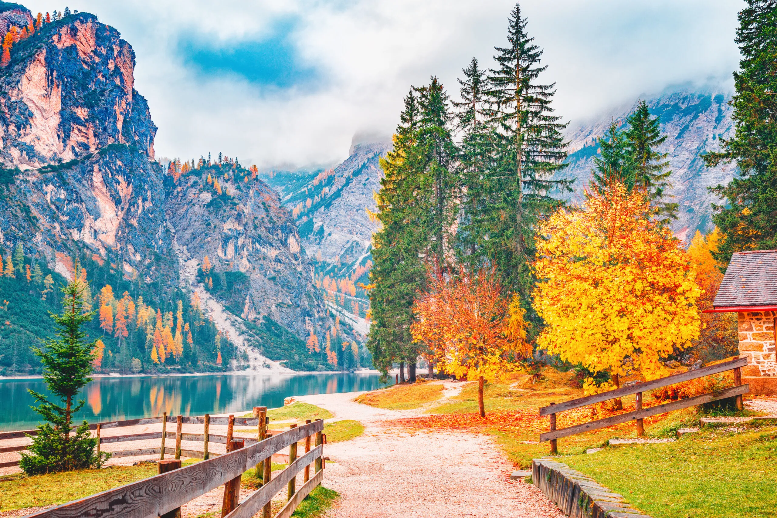 Осенний пейзаж озера Брайес - lago di Braies на фоне Альп в Южном Тироле в Италии. Европейское знаменитое и очень популярное туристическое направление. Осенний пейзаж с желтыми листьями деревьев на берегу озера.